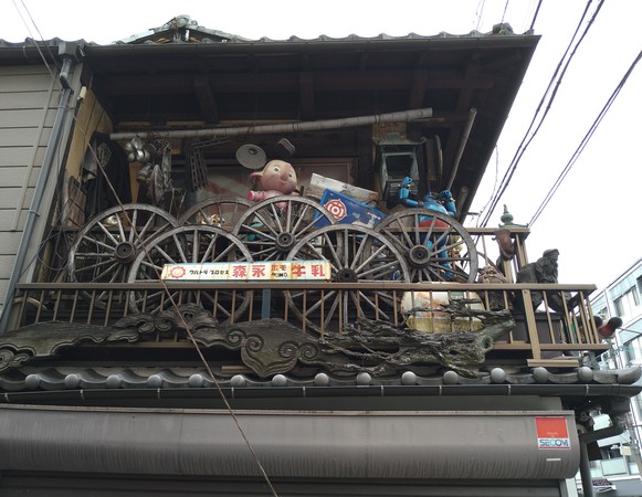 Bland bråten märks ett par maneki-neko, sex vagnshjul, en Tetsujin 28 och en reklamskylt för Morinagas ultrahomogeniserade (“HOMO”) komjölk.