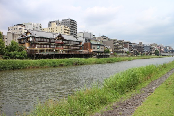 Till vänster Tsuruse (鶴清), ett värdshus med fin restaurang. I mitten av bilden Atoll Terrace Kamogawa, en bröllopslokal med ett stort fönster mot floden och ett praktfullt blomsterarrangemang i fönstret. Till höger, och i fonden, andelslägenheter.